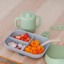 Children's meal set with divided tray, cup, and spoon on a wooden table.