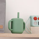 Green silicone cup with straw on a wooden shelf with a neutral background