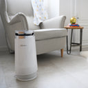 White air purifier beaba on a tiled floor with a sofa and decorative items in the background