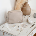 Beige cosmetic bag with BEABA branding on a wooden surface with pampas grass decor.