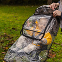 Baby in a transparent stroller cover with a blurred green outdoor background