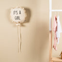 Baby shower decoration with 'It's a Girl' balloon, baby clothes, and 'Baby Necessities' bag on a shelf.