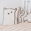 Decorative pillows shaped like a bear, cactus, and cloud on a bed with striped bedding.