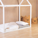 White children's house-shaped bed in a room with beige walls and wooden floor.