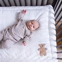 Baby lying on a white blanket with a teddy bear design in a crib.