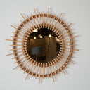 Round wooden mirror with a wicker frame on a light gray wall