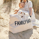 Woman and child sitting on sand with a 'FAMILY BAG' bag in front