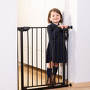 Child standing next to a black metal safety gate indoors.